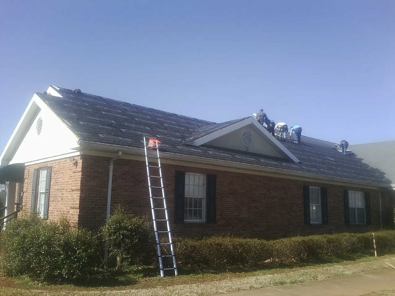 Crew tearing shingles off a brick ranch roof with a ladder set — Emergency Roof Repair work by our crew in Lyme