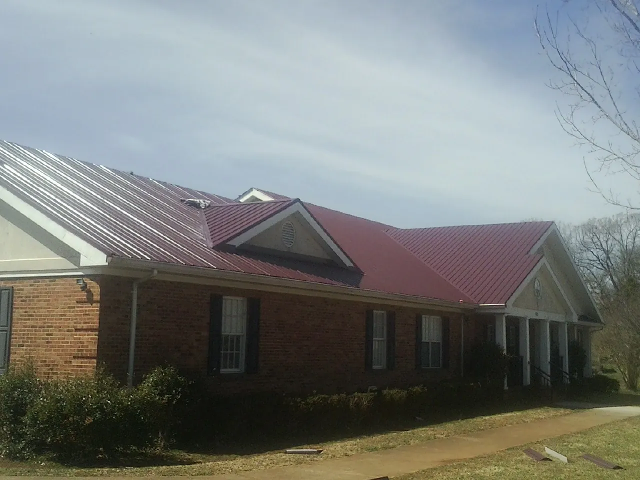 Red metal roof with gabled entries on a long brick building, from a Hail Damage Roof Repair job in Lyme