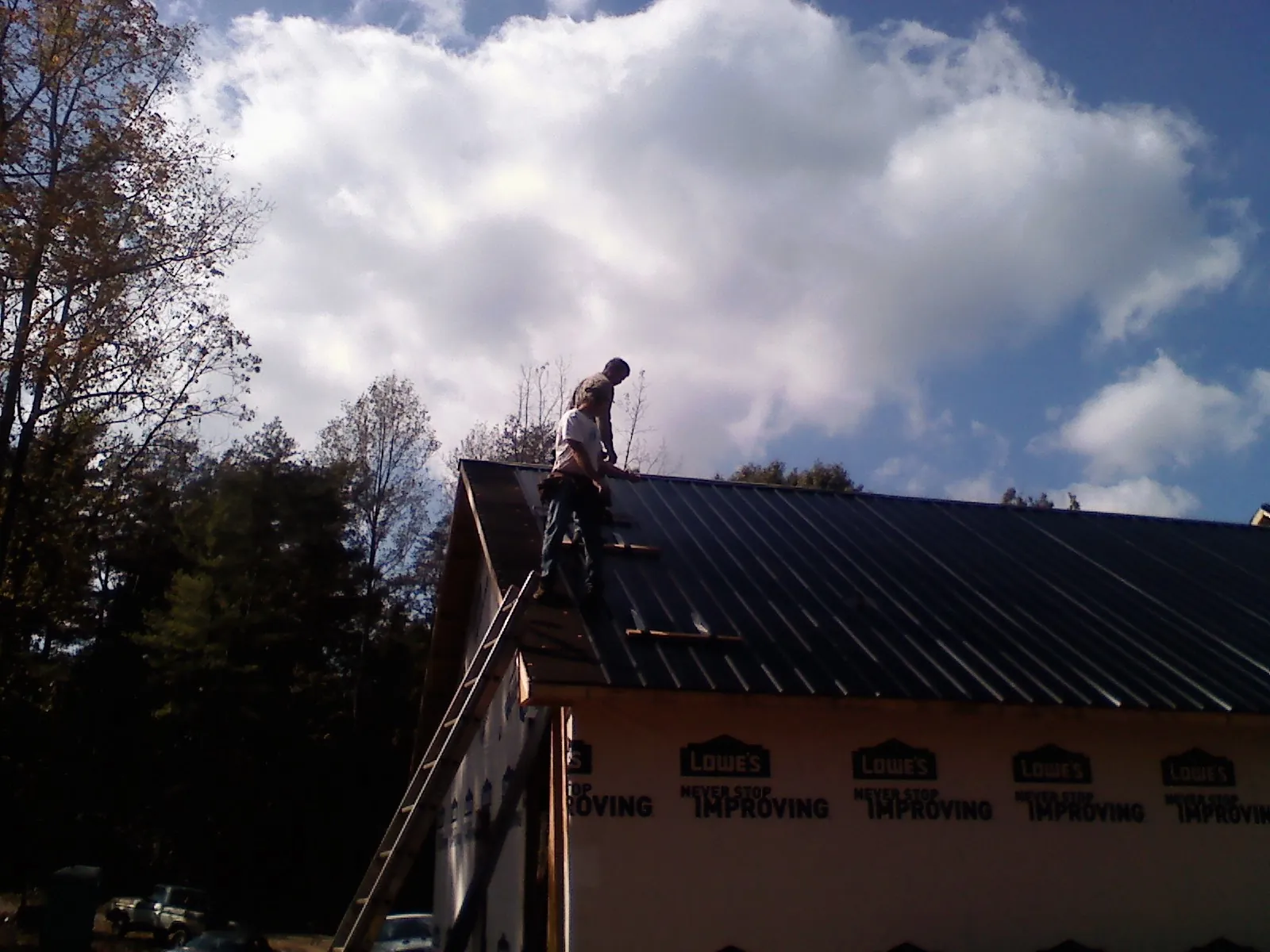 Roofer fastening dark metal panels high against a cloudy sky, from a Roof Inspection job in Lyme